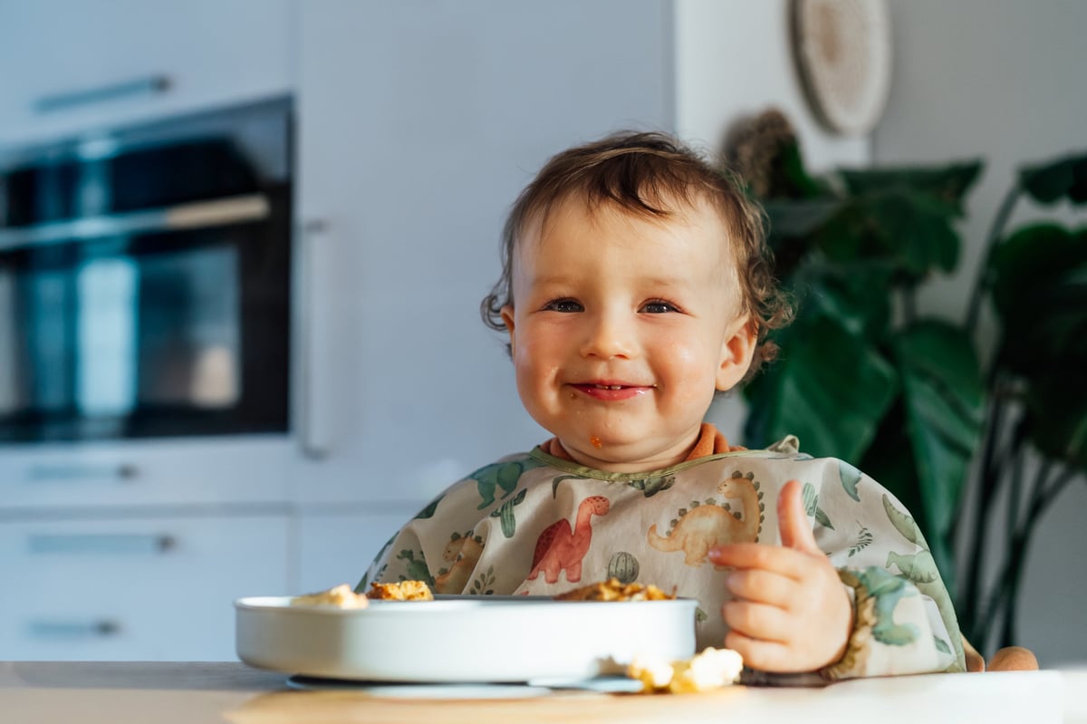 Bebé feliz comiendo solo con técnica baby-led weaning (BLW), explorando la comida con sus propias manos